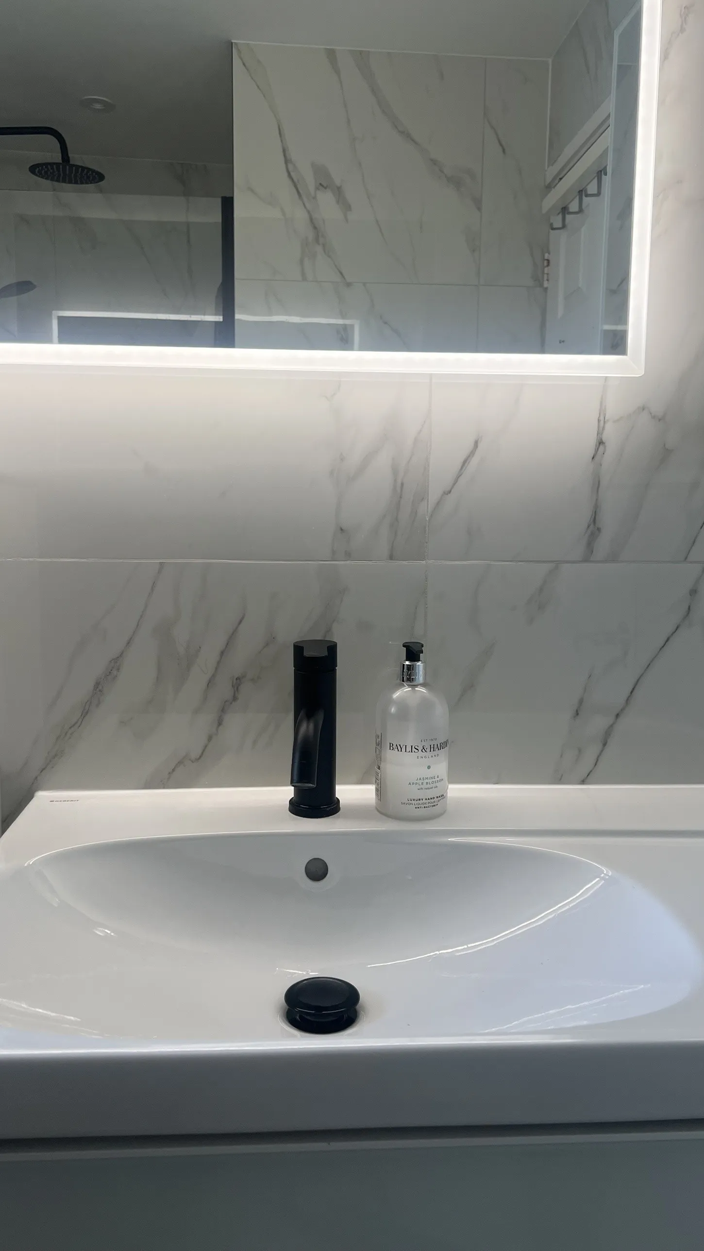 Basin with matt black tap beneath a backlit mirror