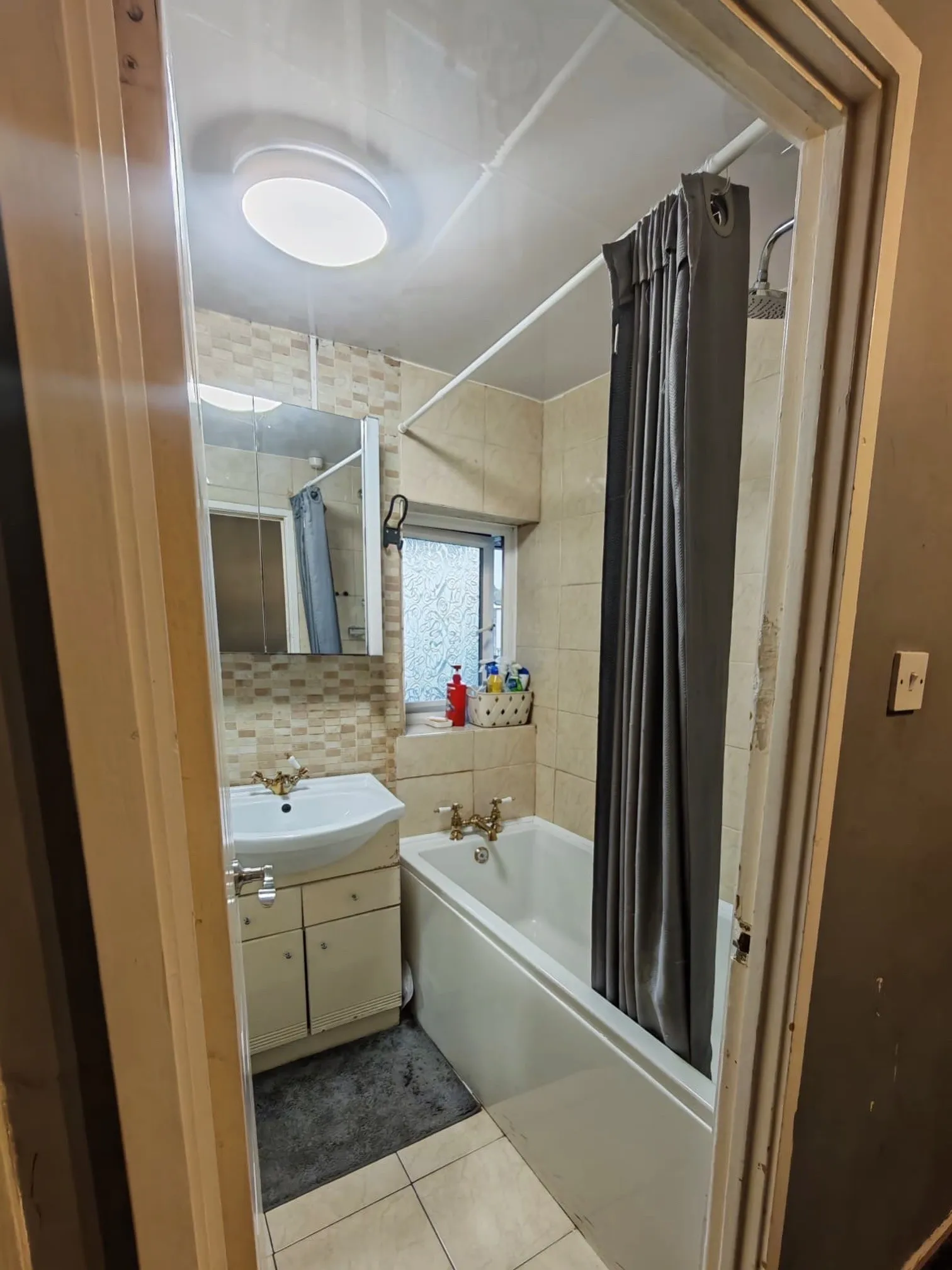 Before: beige mosaic tiles, brass taps and a bath with a shower curtain
